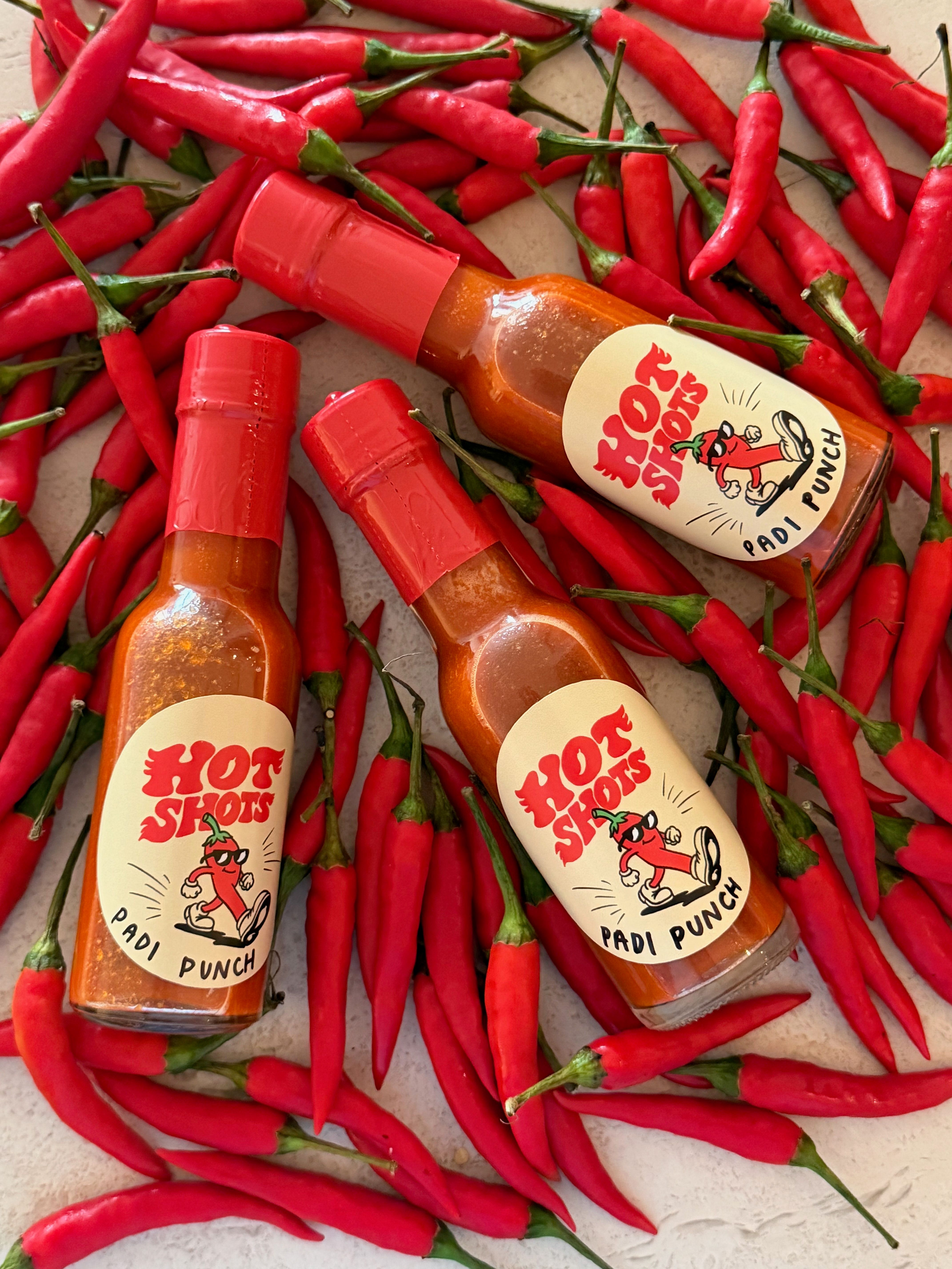 Bottles of Hot Shots Padi Punch laid in a bed of fresh red chilli padi