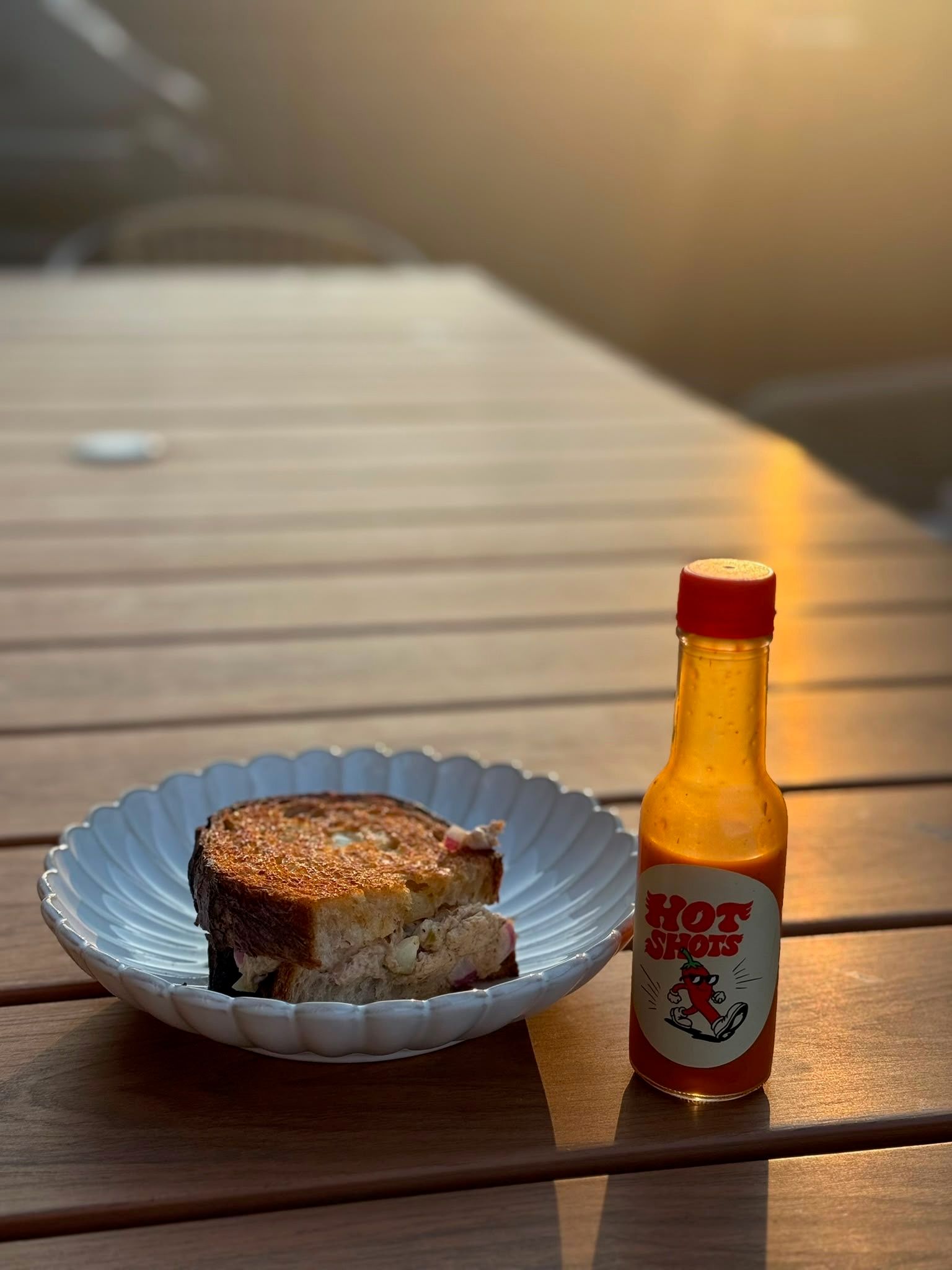 A bottle of Hot Shots beside a toasted sandwich on an outdoor table at sunset